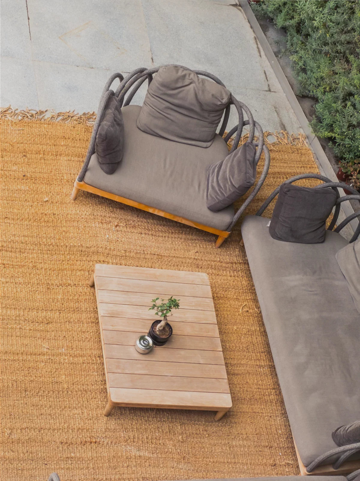 Cozy outdoor lounge setup featuring a natural fiber 6x9 rug, wooden coffee table with a small bonsai plant, and stylish cushioned seating, creating a warm and inviting patio space.