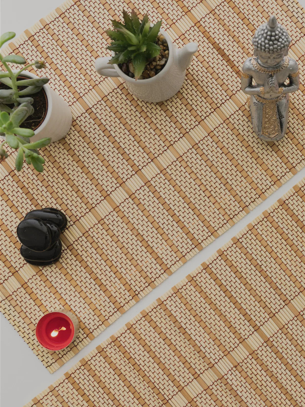 Natural bamboo rug with a woven pattern, styled with small potted succulents, a Buddha figurine, and zen-inspired decor items on a light surface.