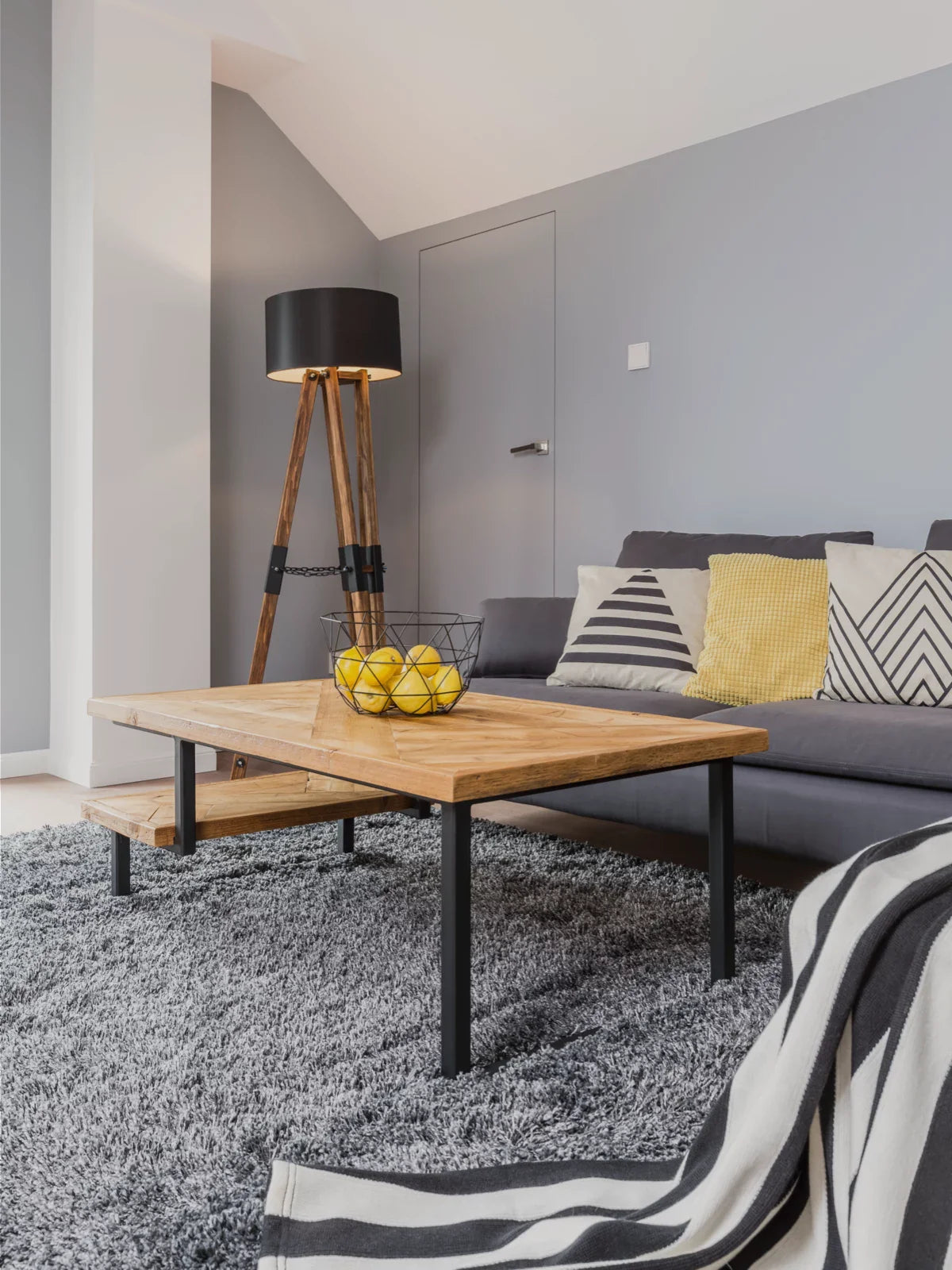 Modern living room with a plush gray rug, a rustic wooden coffee table, and a cozy gray sofa accented with yellow and patterned cushions for a stylish contrast.