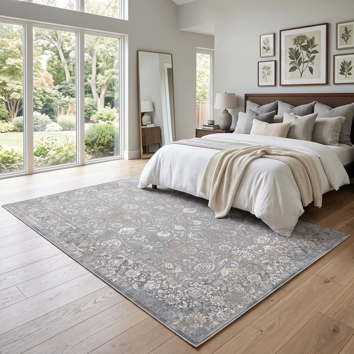 Ein großer rechteckiger Teppich mit einem kunstvoll auf alt getrimmten Blumenmuster in Grau-, Beige- und Weißtönen, präsentiert auf einem hellen Holzboden in einem modernen Schlafzimmer.