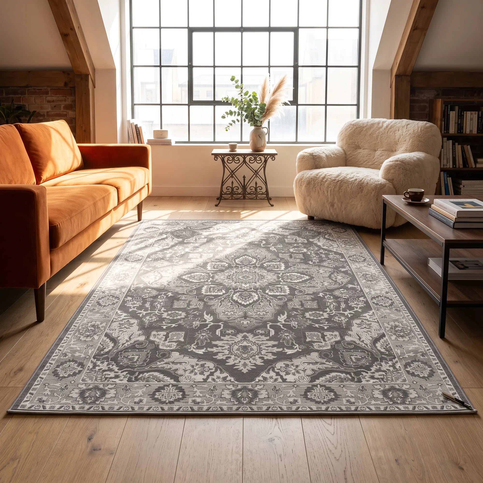 Ein großer rechteckiger Teppich mit einem filigranen traditionellen Medaillonmuster in Grau und Cremeweiß, arrangiert in einem hellen, modernen Wohnzimmer mit Holzboden, einem orangefarbenen Sofa und einem cremefarbenen Sessel.